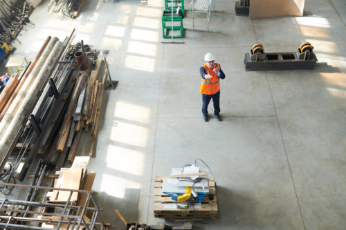 Directly above view of senior construction manager in hardhat and orange vest guiding process of building and using radio while talking to worker at construction site